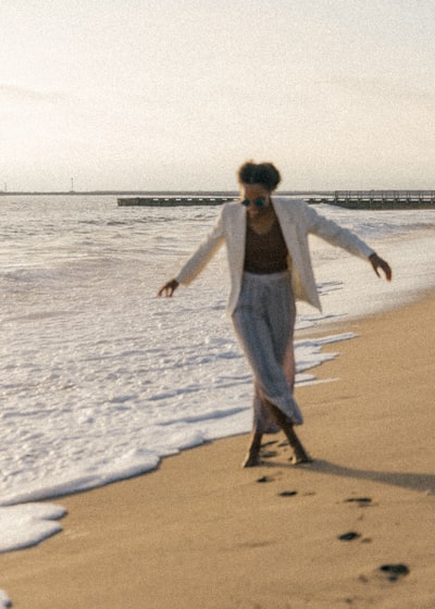 穿着白色长袖衬衫和灰色裤子的女人白天在沙滩上散步
